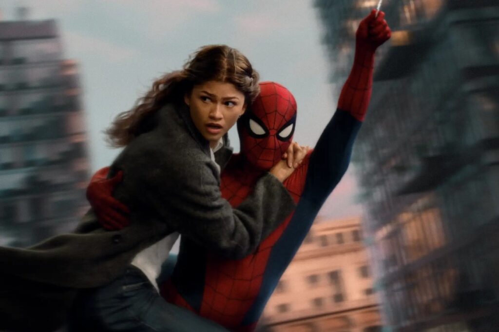 Classic swing-and-save energy returns, but the emotion is different now that MJ does not remember the boy under the mask. Alt text: Spider-Man carrying Zendaya’s MJ through the air above city buildings, her coat flying as he reaches upward with a web line in Spider-Man Brand New Day 2026.