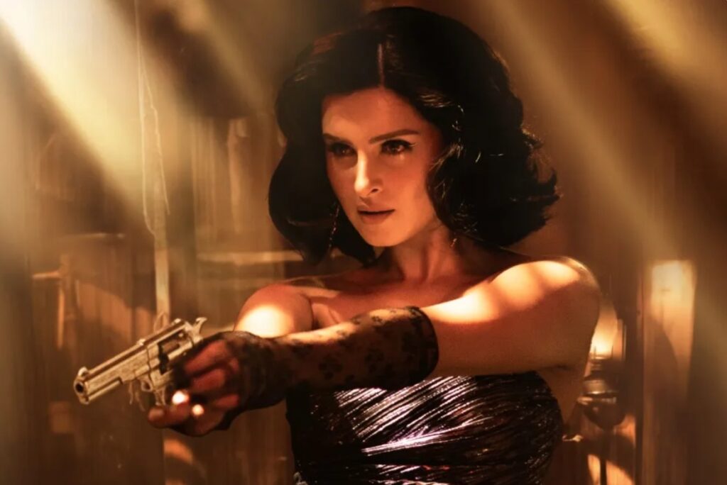 Tara Sutaria as Rebecca Almeida in Toxic, pointing a revolver in a warmly lit, vintage interior. The still captures the character’s mix of elegance and threat that several reviews noted as one of the film’s stronger supporting turns.