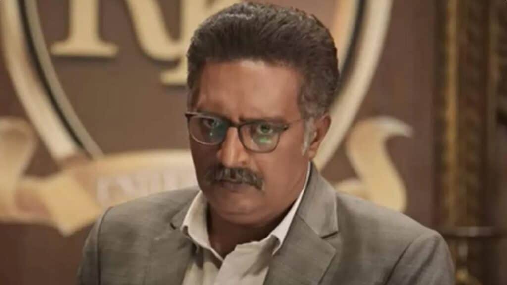 Prakash Raj in a grey suit and glasses, matching the authority he brings to public prosecutor Indrajith Shetty in Drishyam 3.